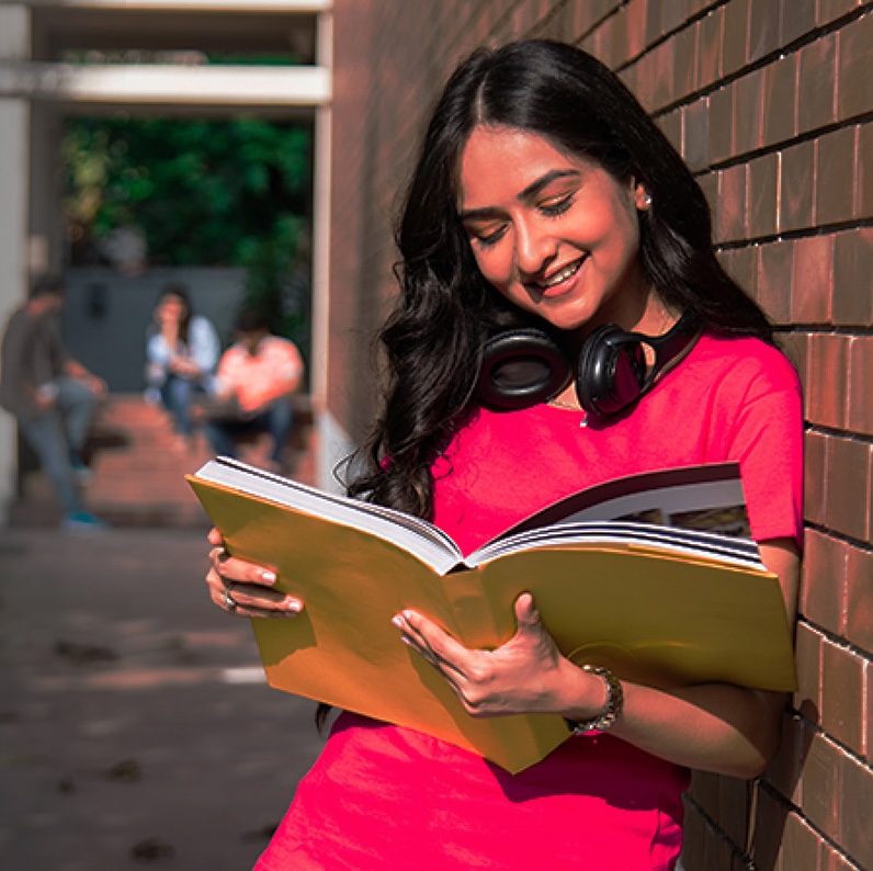 A focused South Asian accounting student smiling while holding a laptop and notebook, modern Colombo skyline architectural light streaming in soft daylight